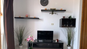 Una sala de estar con televisor, reloj y estanterías llenas de libros y vasos.