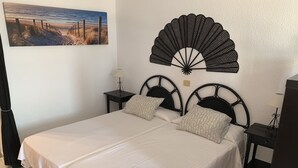 Una cama bien hecha con sábanas blancas, dos mesitas de noche con lámparas y un adorno decorativo sobre la cama.