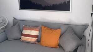 Un sofá gris con tres cojines, un cuadro enmarco de un paisaje y una lámpara de pie.