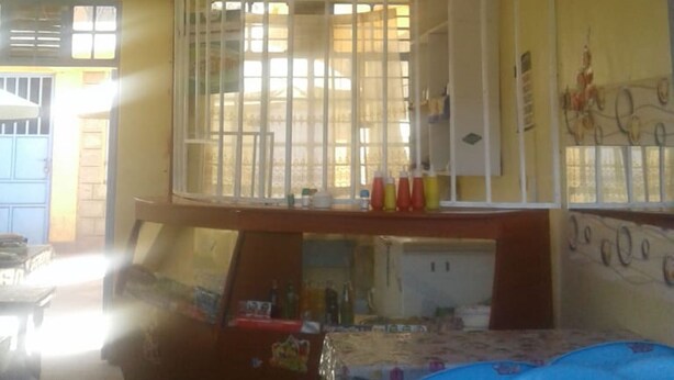 A dining area with tables covered in blue tablecloths, a white partition, and a wall decorated with pictures of food. - Check Point Guest House (Isinya)