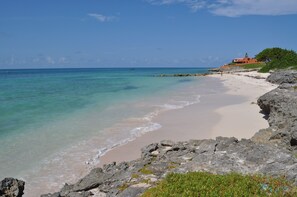 A beach with clear turquoise water, a sandy shore, and rocky outcrops.