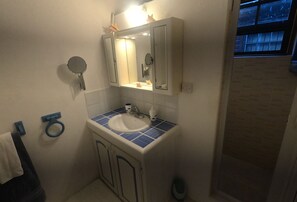 A bathroom with a white sink, blue-tiled countertop, a mirror above the sink, and a window with blinds. - Blue Ocean Villa  in Silver Sands (Silver Sands)