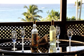 A table with a bottle of rum, a bottle of white wine, and four glasses on a wicker table with a view of the ocean. - Blue Ocean Villa  in Silver Sands (Silver Sands)