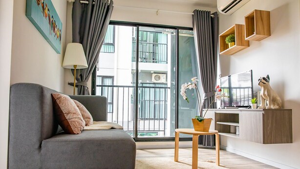 A modern living room with a grey sofa, a small wooden table, a potted orchid, and a dog figurine on a cabinet. - Apartment 450m from BTS with Sky Pool - bkbloft1 (Samut Prakan)