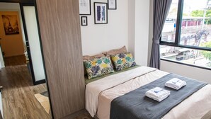 A hotel room with a bed, pillows, a window with a view, and a door leading to another room. - Apartment 450m from BTS with Sky Pool - bkbloft1 (Samut Prakan)