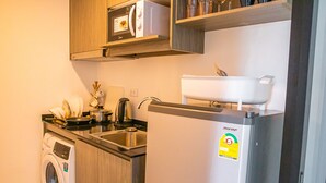 A compact kitchen with a washing machine, a microwave, and a refrigerator. - Apartment 450m from BTS with Sky Pool - bkbloft1 (Samut Prakan)