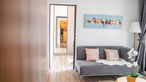 A modern living room with a grey sofa, a painting of birds, and a potted orchid. - Apartment 450m from BTS with Sky Pool - bkbloft1 (Samut Prakan)