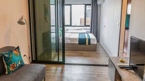 Une chambre d’hôtel moderne équipée d’un lit, d’un canapé, d’une télévision et d’une porte-fenêtre coulissante donnant sur un balcon.