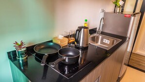 Une petite cuisine équipée avec un plan de travail noir, un évier en acier inoxydable, une bouilloire, une poêle et une petite plante en pot.