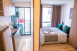 A modern hotel room with a kitchenette, a balcony with a view, a bed with a patterned bedspread, and a cat statue. - Apartment 450m from BTS with Sky Pool - bkbloft5 (Samut Prakan)