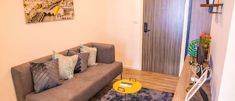 A living room with a grey sofa, a small round table, a painting of a cityscape, and a wooden door.