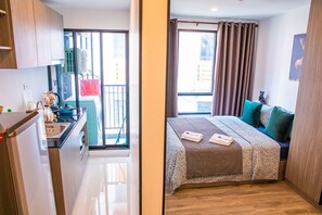 Quarto de hotel moderno com cozinha compacta, varanda com vista, cama com colcha estampada e uma estátua de gato.