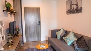Uma sala de estar moderna com um sofá cinzento, uma mesa de centro, uma estante e uma porta com cortina.