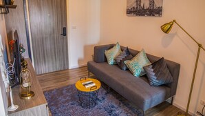 Uma sala de estar moderna com um sofá cinza, almofadas estampadas, uma mesa de centro redonda e um quadro de uma ponte na parede.
