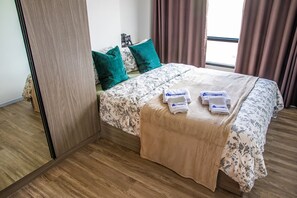 A neatly made bed with floral bedding, two green pillows, and a beige throw blanket.