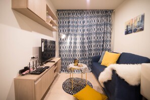 A modern living room with a blue sofa, a yellow pillow, a small round table, and a TV on a wooden cabinet. - Apartment BTS On Nut, Convenience Store Nearby - bkmono3 (Bangkok)
