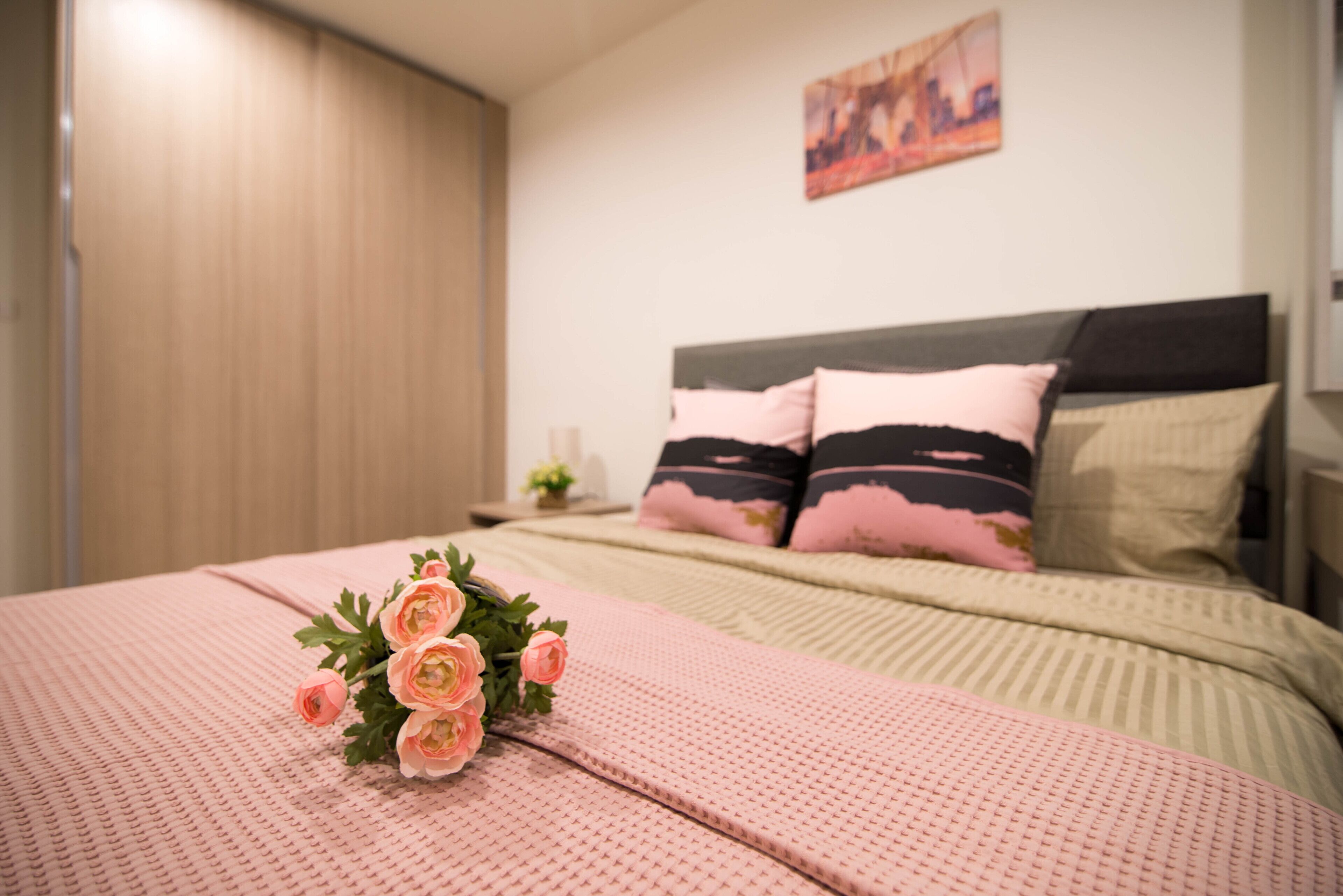 Ein ordentlich gemachtes Bett mit rosa Bettwäsche und einem Blumenstrauß.