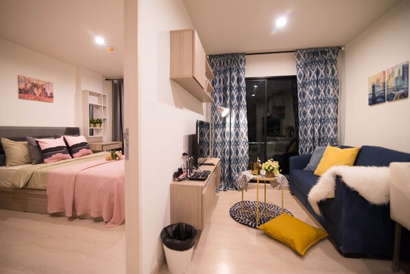 A modern living room with a bed, sofa, and a small table with a lamp.