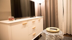 A room with a flat-screen TV on a white dresser, a small table with a remote control, and a lamp. - Community Apartment - bkbhce12 (Bangkok)