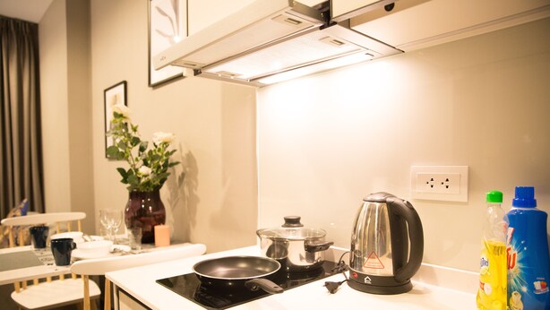 A kitchen with a stove, a kettle, and a table with chairs. There are also two bottles of dish soap on the counter. - Community Apartment - bkbhce12 (Bangkok)