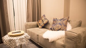 A beige sofa with patterned cushions, a small round table with a checkered tablecloth, and a remote control on it. - Community Apartment - bkbhce12 (Bangkok)