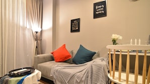 Ein gemütliches Wohnzimmer mit einer Couch, einem kleinen Tisch mit Tablett, einem Babybett und Wanddekorationen.