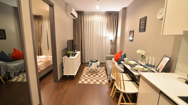 Ein kleines Hotelzimmer mit einem Bett, einem Schreibtisch, einem Stuhl, einem kleinen Tisch und einem karierten Teppich.
