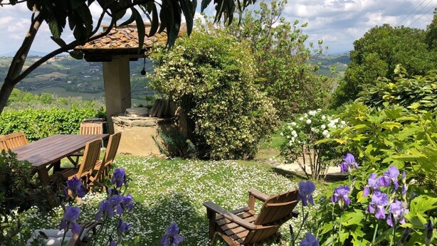 Un patio con una mesa y sillas de madera, rodeado de exuberante follaje y flores.