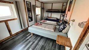 A compact RV bedroom with a bunk bed, a small wooden bench, and a window with curtains.