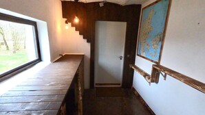 A narrow hallway with a wooden bench on the left, a door at the end, and a map on the right wall.