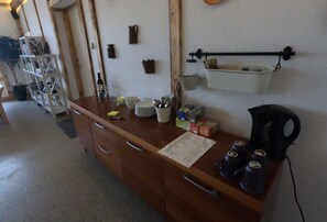 A kitchen with wooden cabinets, a countertop with various kitchen items, and a hanging shelf with a kettle. - Billund BnB (Billund)