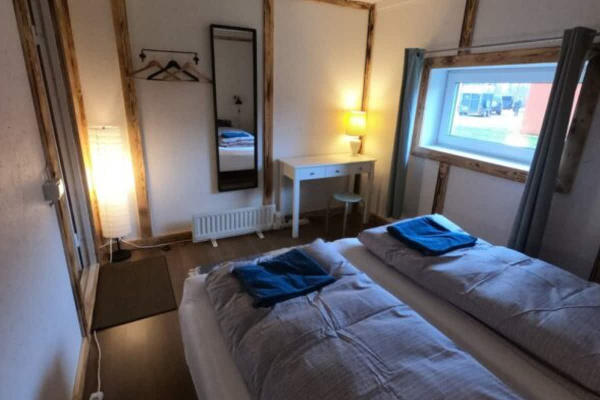 Une chambre avec deux lits, un bureau, un miroir et une fenêtre.