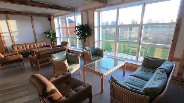 A spacious room with multiple seating options including sofas and chairs, a glass coffee table, and large windows offering a view of the outdoors.
