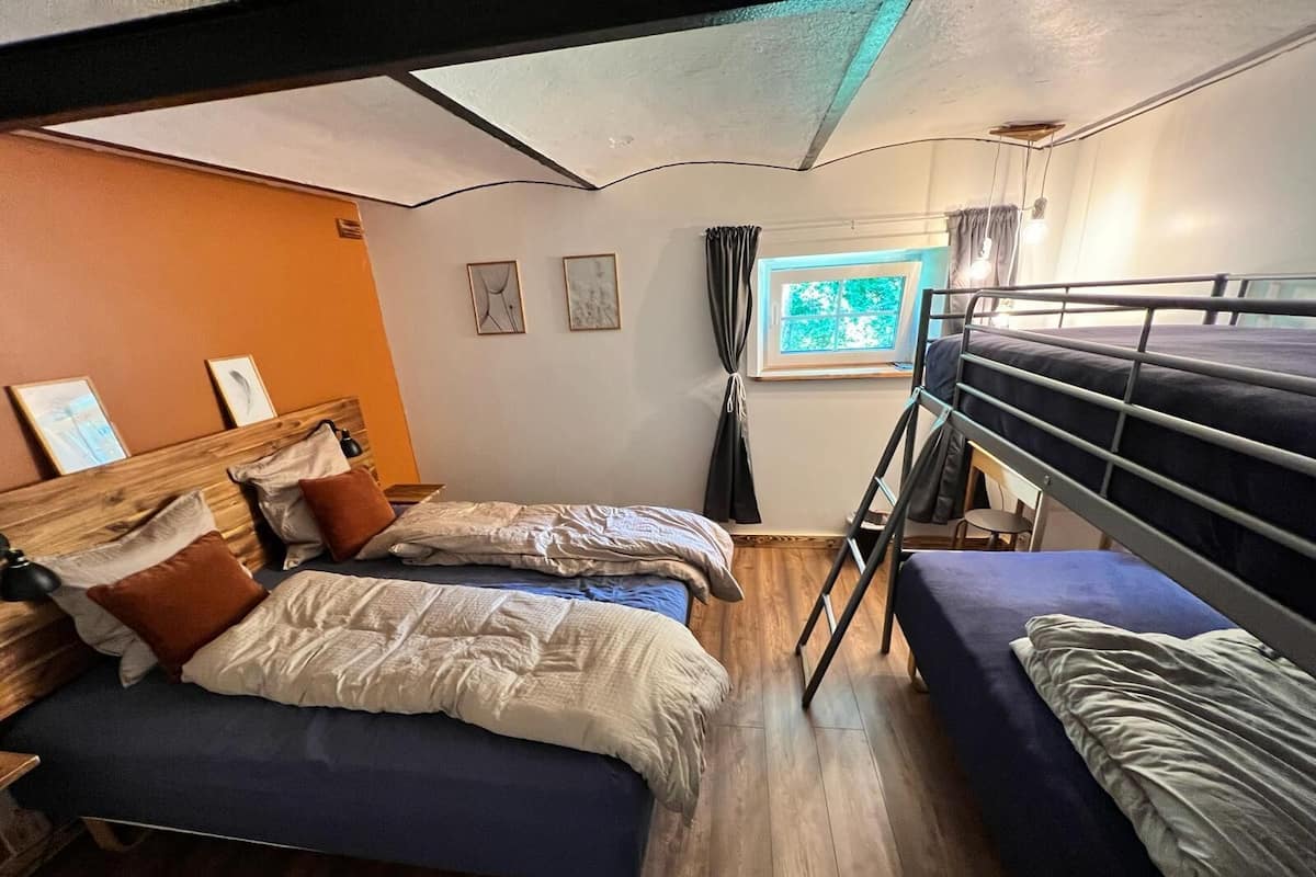 Une chambre de dortoir avec deux lits, un lit superposé, un plancher en bois, une fenêtre avec des rideaux et des œuvres d’art encadrées accrochées au mur.