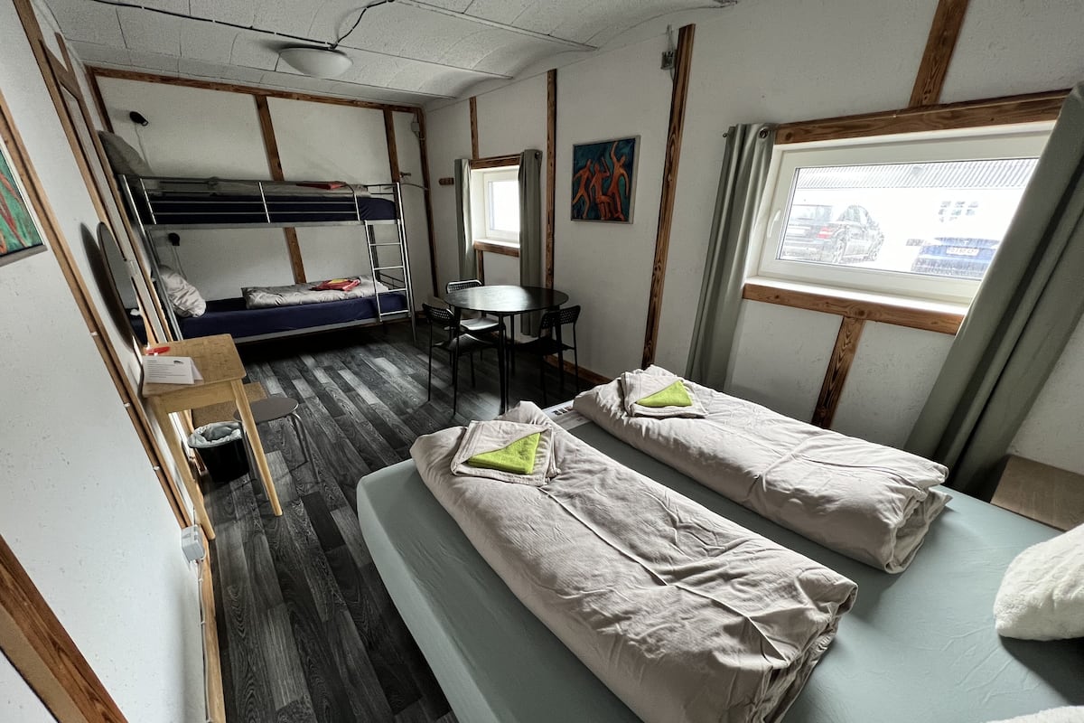 Une chambre de taille modeste, comprenant deux lits simples, un lit superposé, une petite table et une fenêtre.