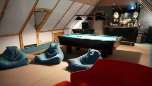 A cozy room with a pool table, bean bag chairs, a red couch, and a bar area with bottles.