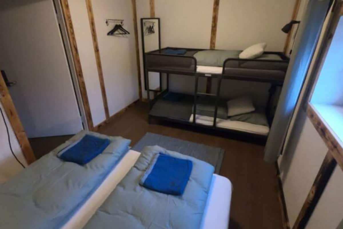 Une petite pièce avec deux lits simples, un lit superposé et une porte.