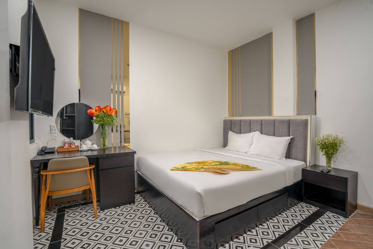 A modern hotel room with a bed, bedside table, and a desk with a chair.