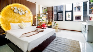 A modern hotel room with a large bed, a decorative headboard, a small side table, a bookshelf, and a view of the city through large windows. - Apro Aparthotel Saigon Center (Ho Chi Minh City)