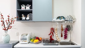 A modern kitchen with a grey countertop, a built-in shelf unit, a small refrigerator, and a sink with hanging utensils. - Apro Aparthotel Saigon Center (Ho Chi Minh City)