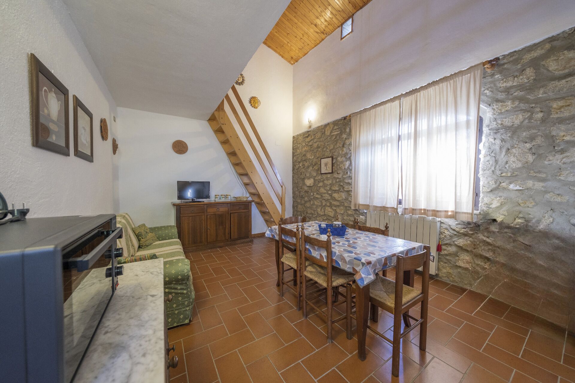 Comedor con una mesa, sillas, televisor y pared de piedra.