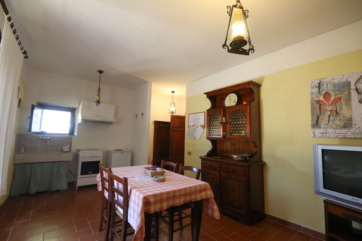 A kitchen with a dining table, chairs, a clock, and a television.