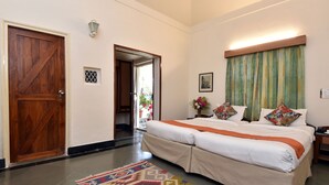 Habitación de hotel con una cama grande, una puerta de madera, un ventanal pequeño, una mesita de noche y una alfombra colorida.