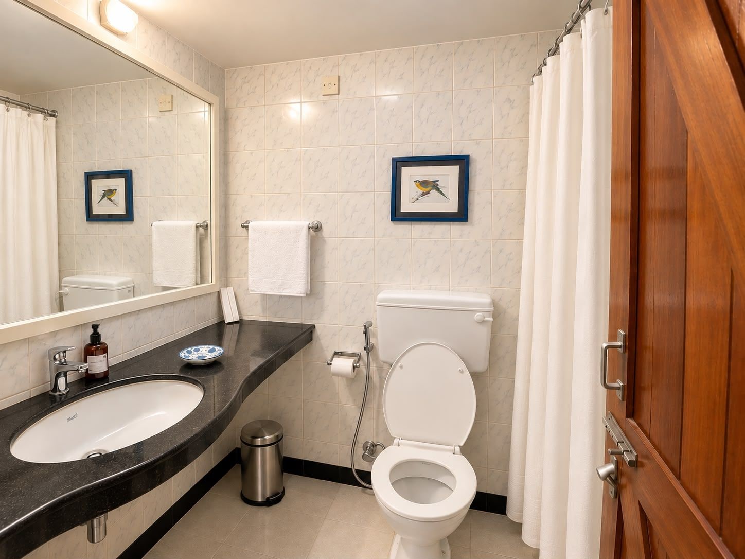 Ein Badezimmer mit einer weißen Toilette, einem Waschbecken mit schwarzer Arbeitsplatte, einem Spiegel und zwei gerahmten Bildern an der Wand.