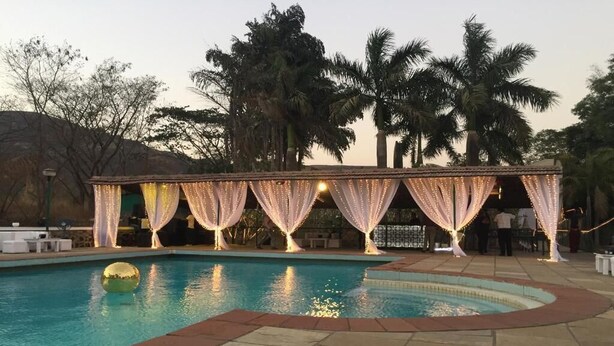 Zona de piscina con un espacio de estar techado decorado con cortinas y luces colgantes.