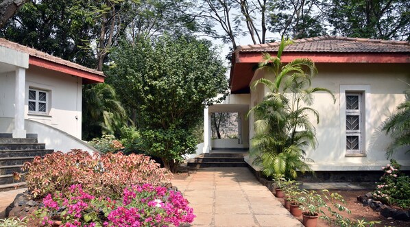 A two-story building with a red roof, surrounded by lush greenery and flowering plants. - Modi's Resort Karjat (Karjat)
