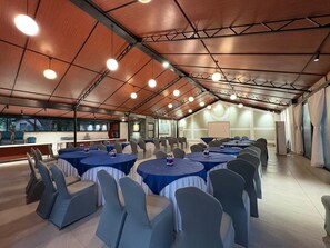 A large indoor space with round tables and chairs, a bar area, and a view through a glass wall. - Modi's Resort Karjat (Karjat)