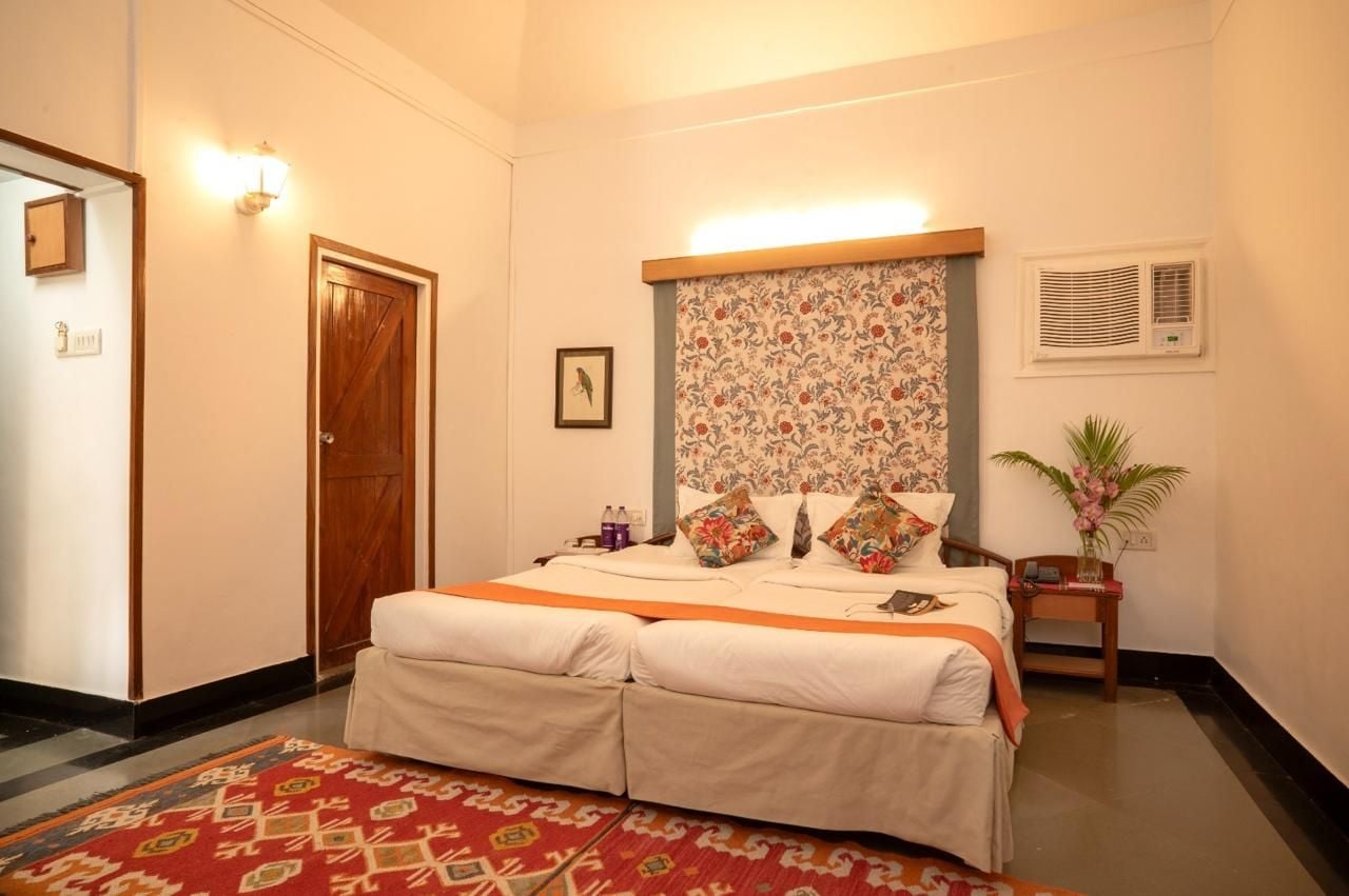 A hotel room with a bed, a bedside table, a nightstand, a wall-mounted air conditioning unit, a door, and a patterned curtain.