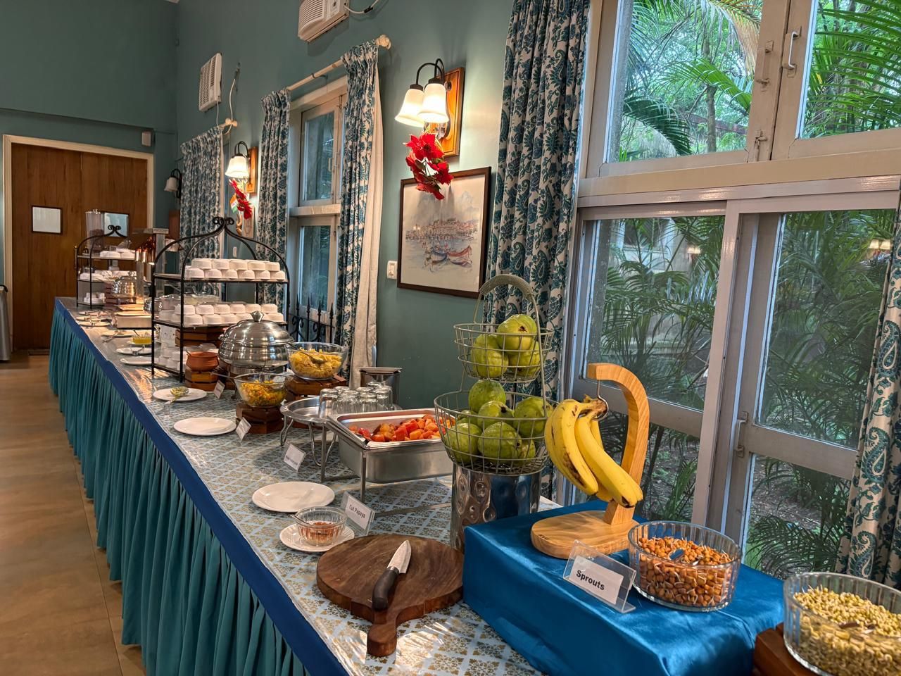 A buffet setup with various food items and a view of greenery outside.