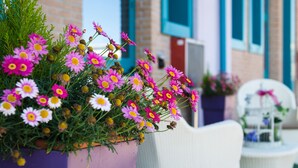 En potte med blomsterarrangement i pink og hvide blomster foran en bygning med blå vinduer og en dør.